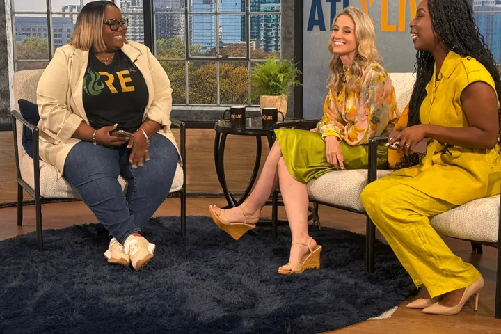 Kayla Life on the set of ATL Live, seated across from the two hosts with the Atlanta skyline behind them