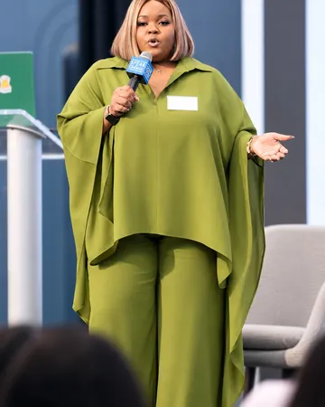 Kayla Life speaking into a microphone on stage, hand open toward the audience