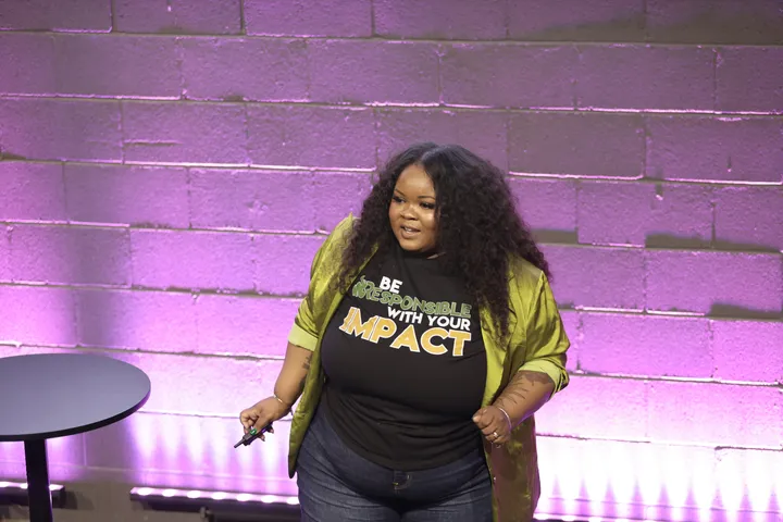 Kayla Life presenting on a purple-lit stage in a shirt reading Be Responsible With Your Impact