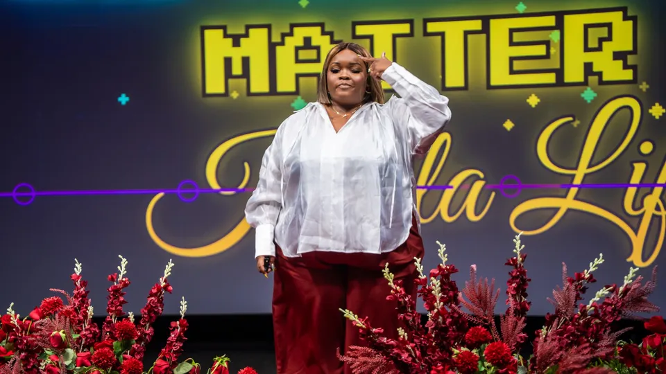 Kayla Life on the TEDxBuckheadAve stage, tapping her temple in front of a sign reading Matter and her name in script